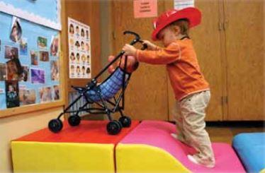 A boy wearing a firefighter hat and pushing a stroller 